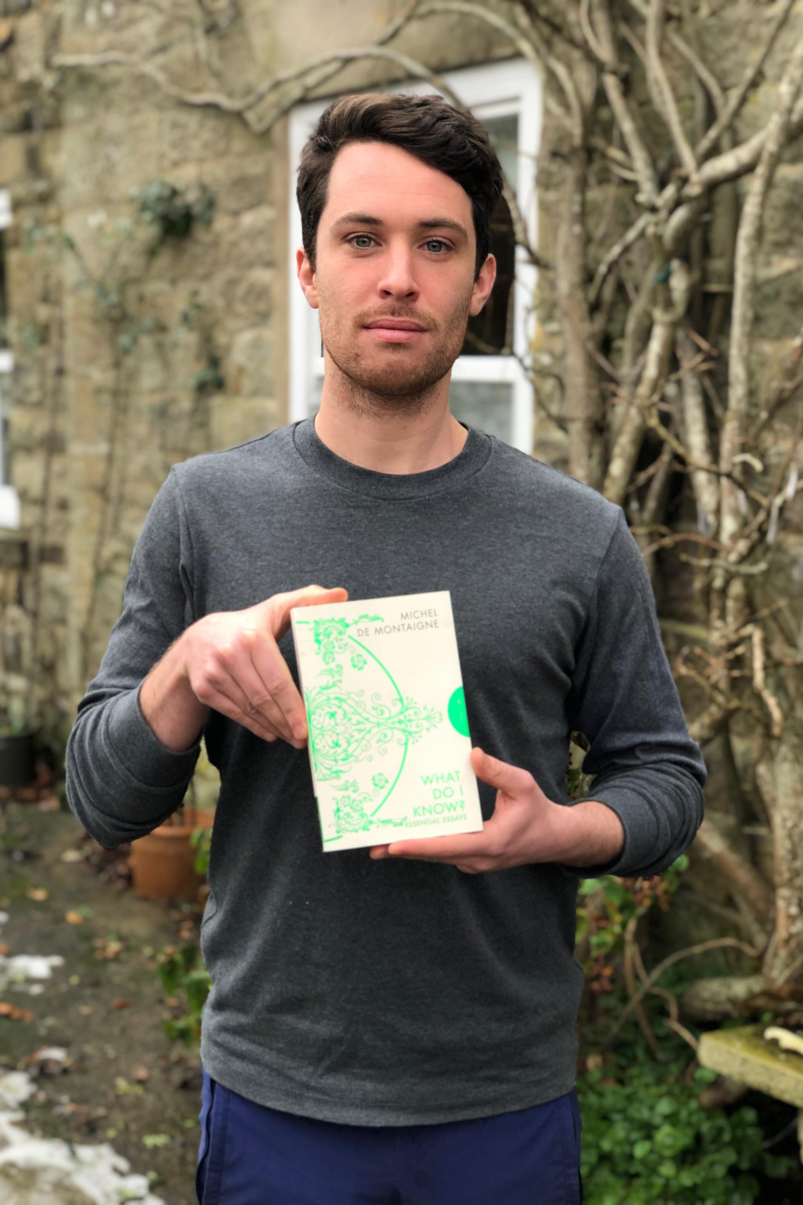 Man holding a green map outdoors with a building and trees in the background
